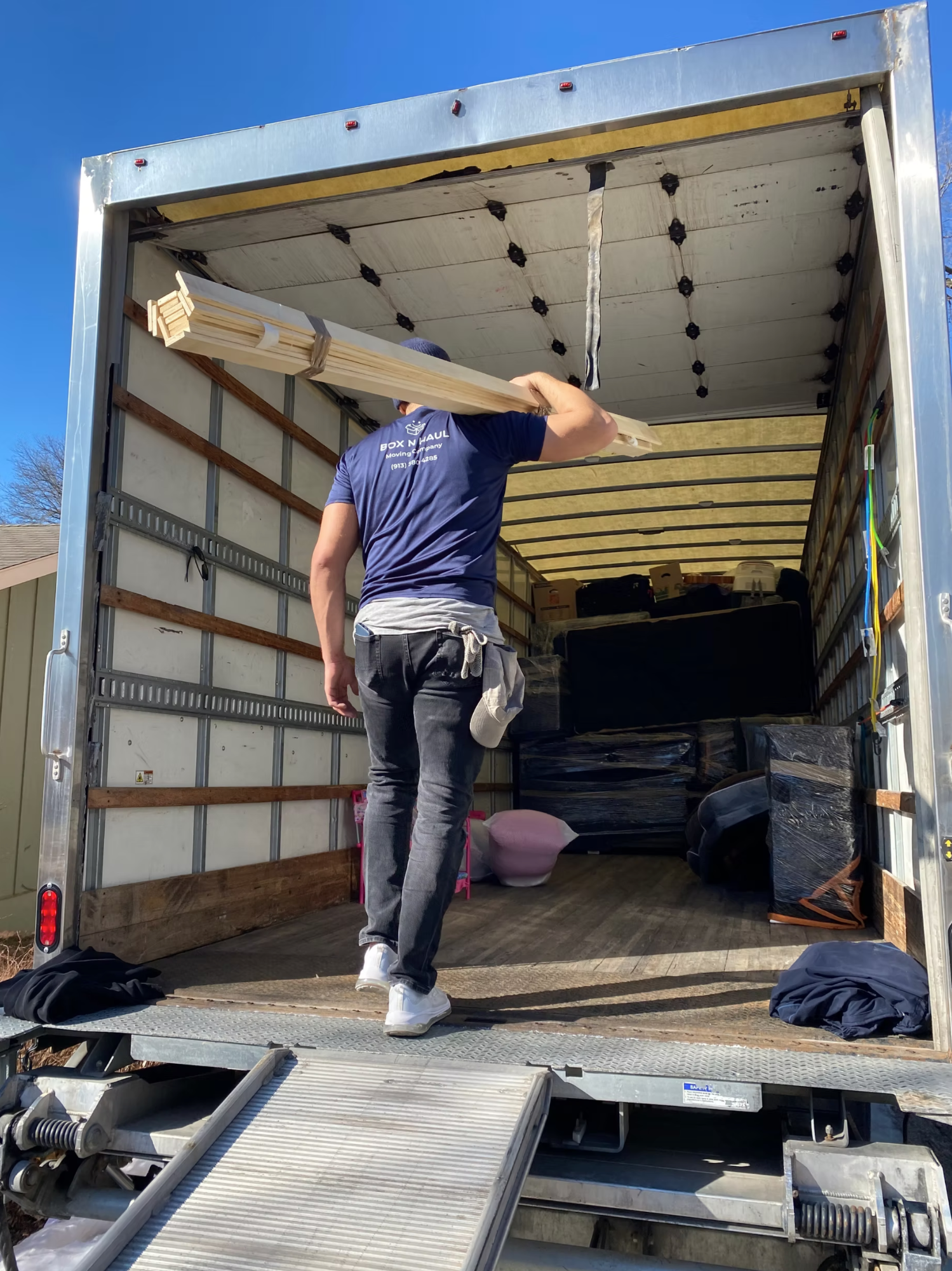 Box N Haul mover loading wrapped bed frame rails into the back of the moving truck on a clear day.