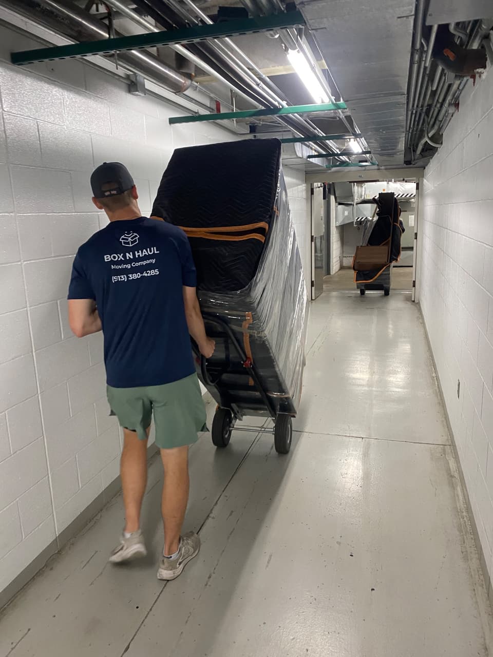 Box N Haul mover transporting wrapped office furniture on a dolly through a service corridor