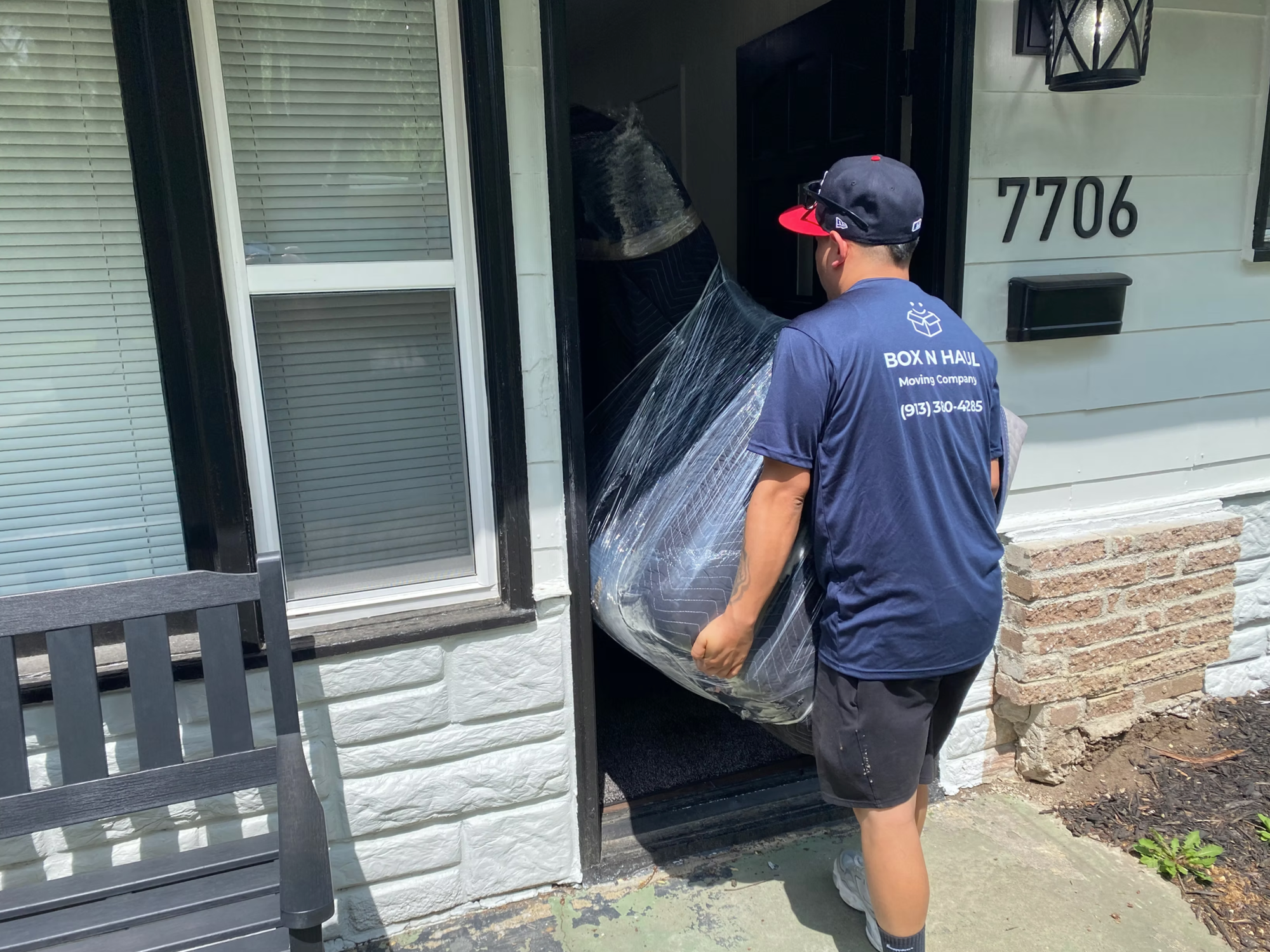 Box N Haul mover carrying a shrink-wrapped mattress through the front door of a home.