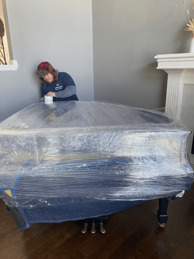 Box N Haul mover wrapping a grand piano in a living room