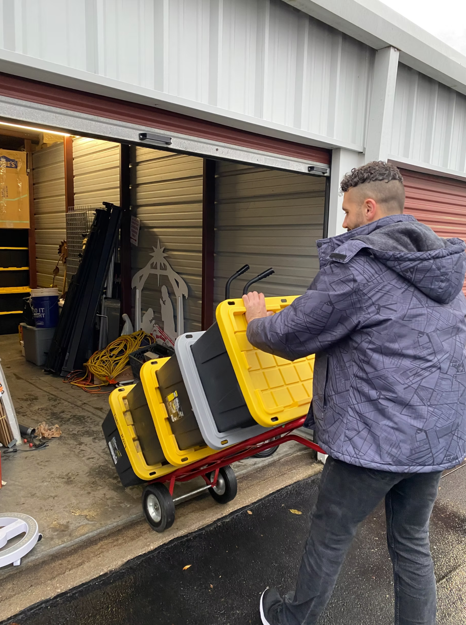 Box N Haul mover wheeling a stack of large storage totes on a dolly outside a storage unit.