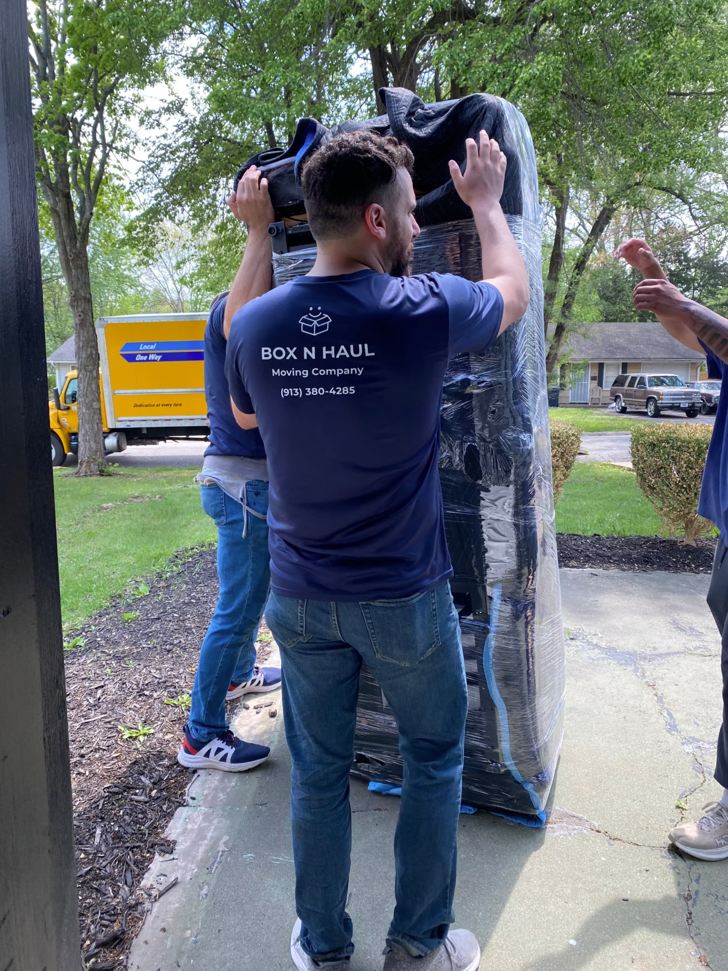 Box N Haul crew carrying a tall shrink-wrapped item up a walkway with the moving truck parked behind them.