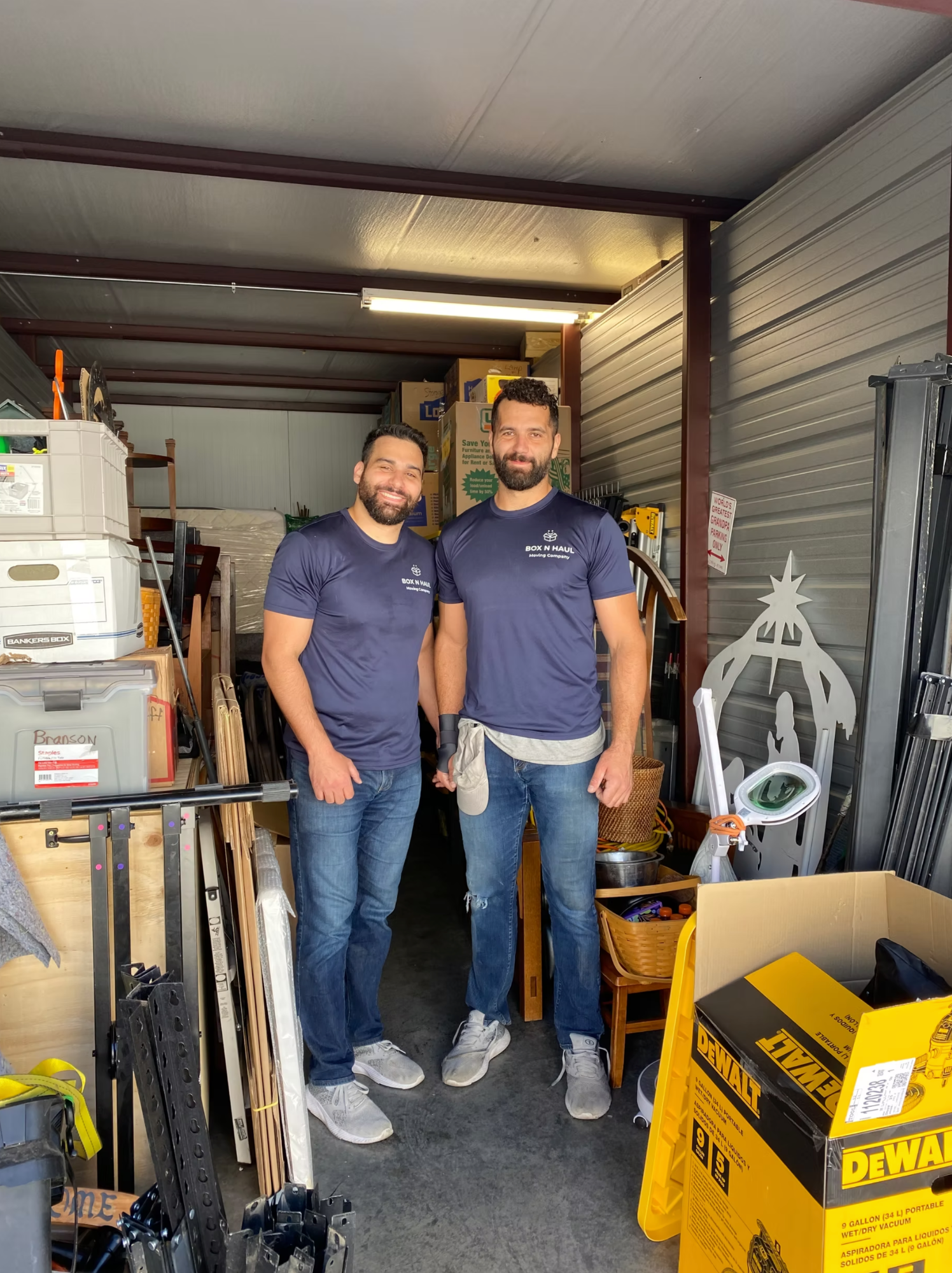 Two smiling Box N Haul movers standing in a packed storage unit during a move.