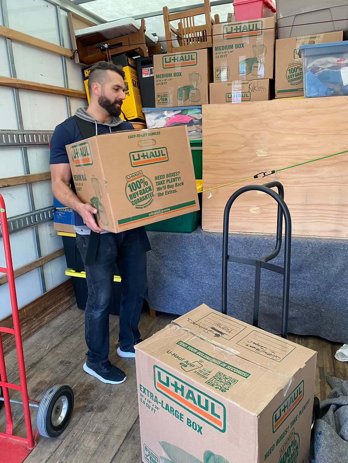 A Box N Haul mover carrying a labeled U-Haul box into a fully loaded moving truck